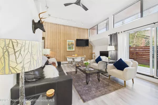 Living room with a wood-paneled wall, modern seating, and glass doors to a deck.