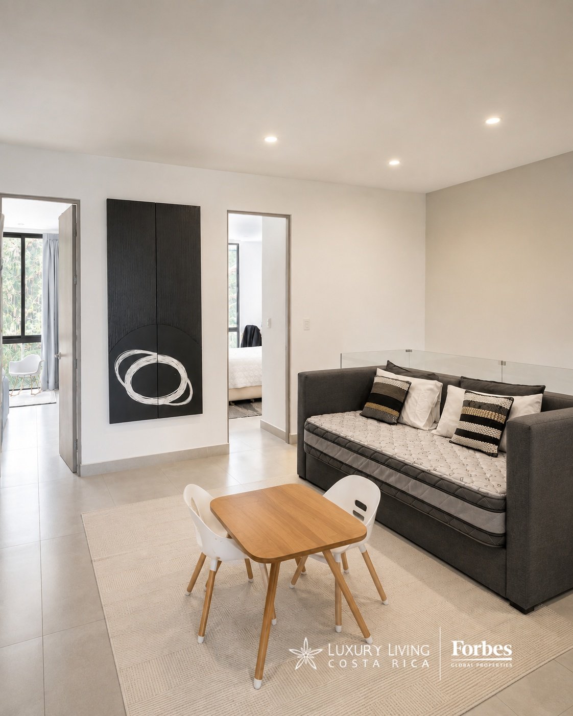 Open-plan living area with a gray sofa, wooden dining table, and doorways to adjoining rooms.