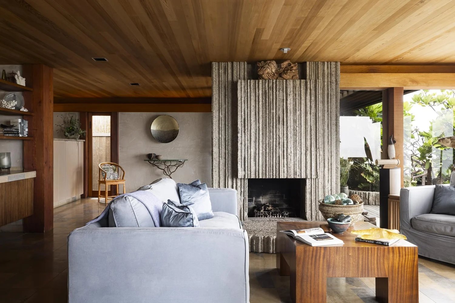 Living room of the Kravis Residence with a wood ceiling and a fireplace clad in vertically textured concrete.