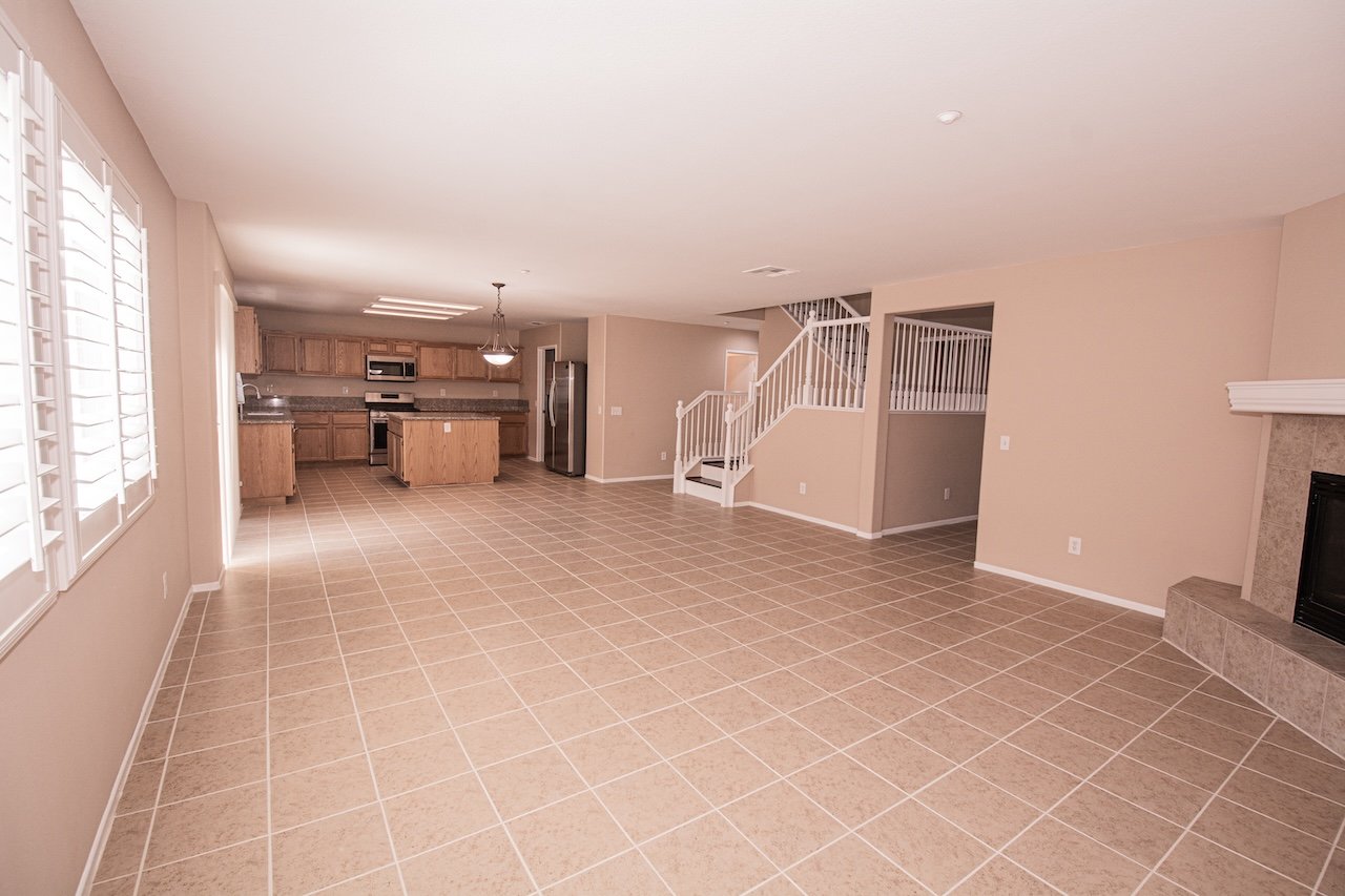 Empty tiled living room with a kitchen, staircase, and fireplace.