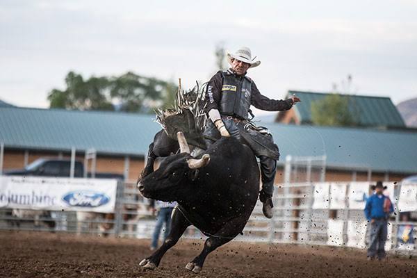 A cowboy rides a bucking black bull in a dirt rodeo arena.