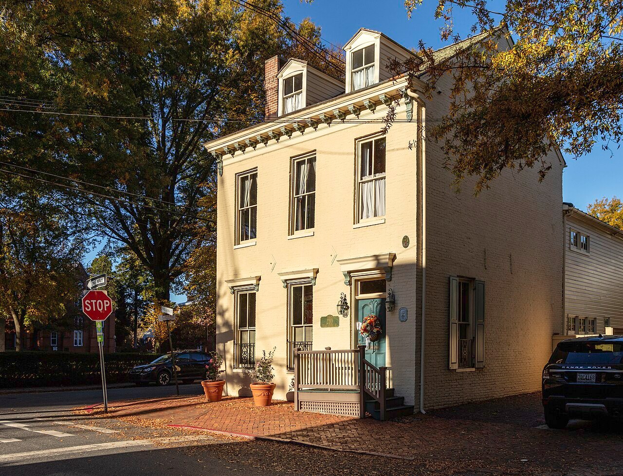 Cream brick historic home with dormers, decorative cornice, blue door, and a small corner porch.