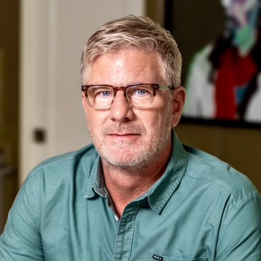 Mark Meyer wearing glasses and a teal shirt, with a softly blurred interior behind him.