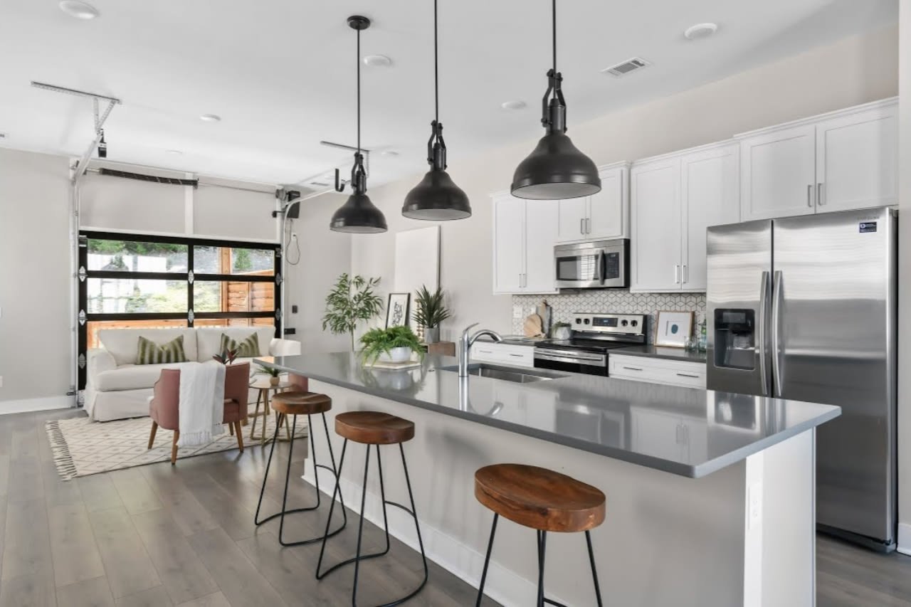 Open-plan kitchen with a large gray island, wooden stools, and a glass-paneled garage door.
