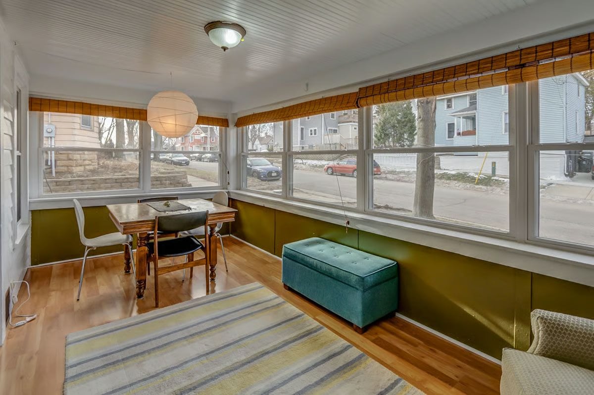 Bright enclosed sunroom with a dining table, broad windows, and teal bench.