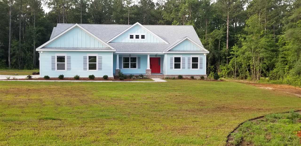 A blue house featuring a red door, surrounded by a lush green lawn.