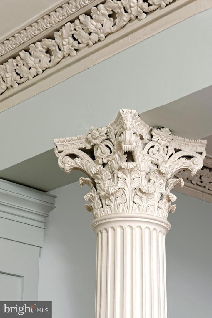 Ornate white Corinthian column with carved foliage beneath decorative ceiling molding.