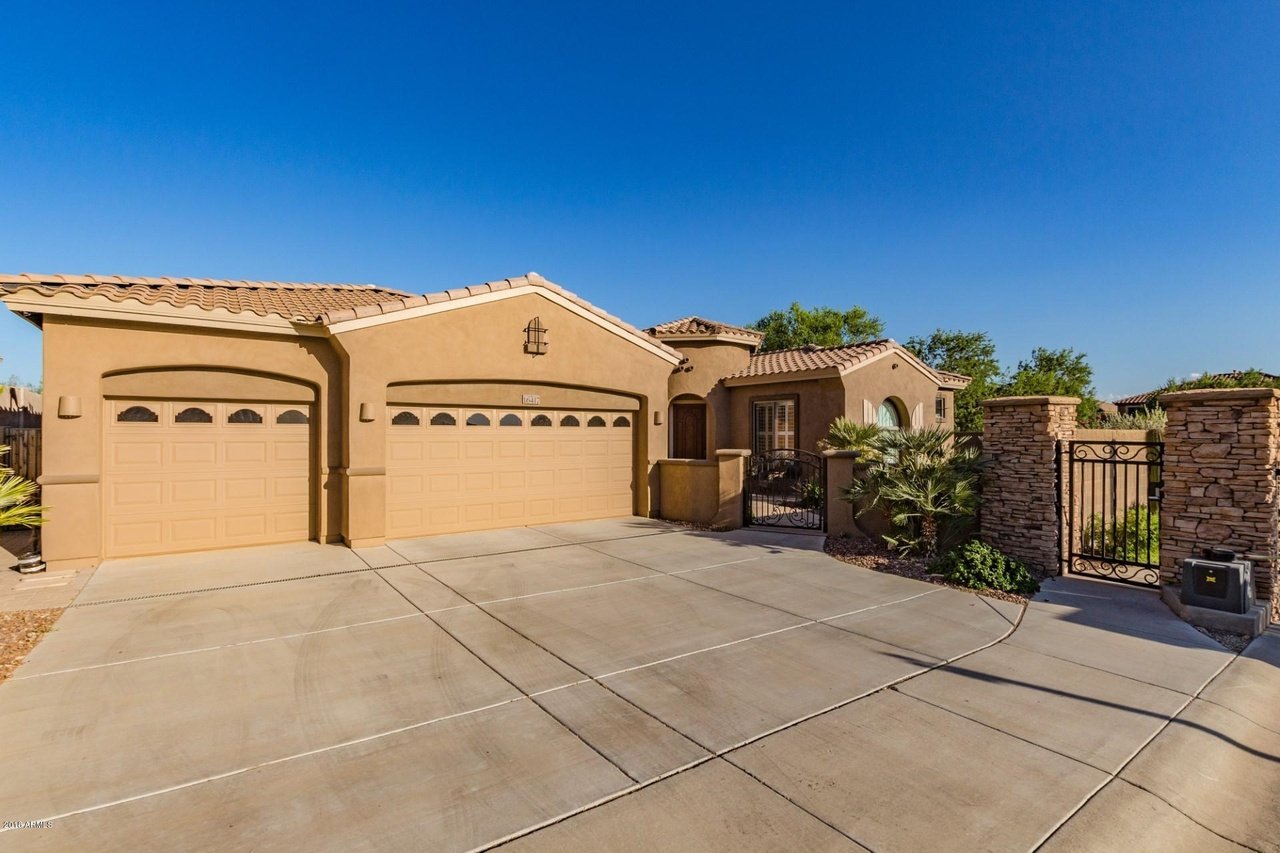Stucco home with two garage doors, tiled roof, broad driveway, and gated entry.