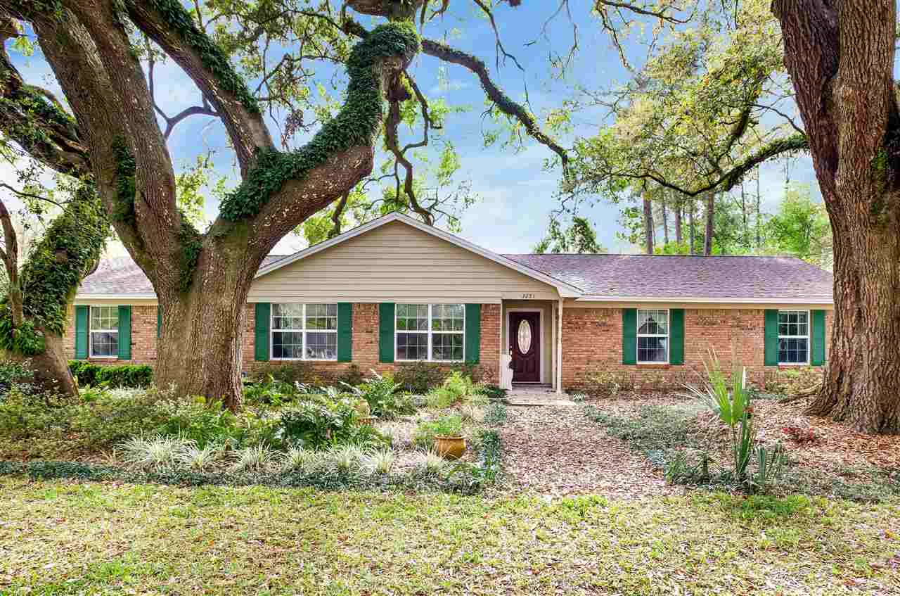 A charming brick home featuring green shutters, surrounded by lush trees, creating a serene and inviting atmosphere.