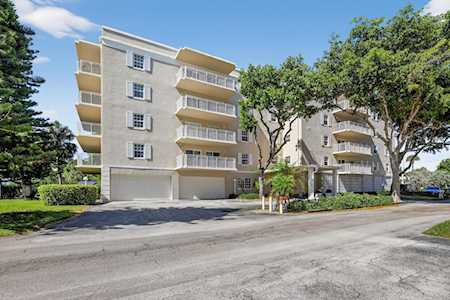 Condominium building with stacked balconies, mature trees, and a street in front.