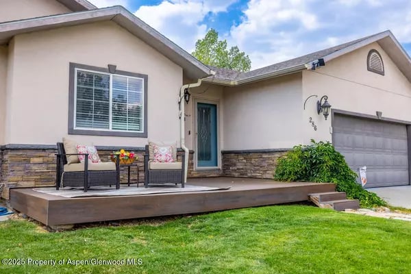 Single-story stucco home with stone veneer, an attached garage, and a raised porch with two chairs.