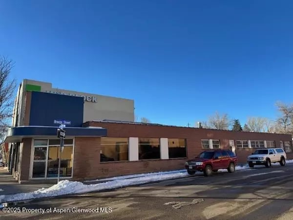 Commercial building with a blue entrance canopy and parked vehicles along a snowy street.