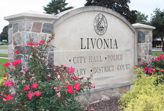 Livonia municipal sign listing City Hall, Police, Library, and District Court, surrounded by flowers.