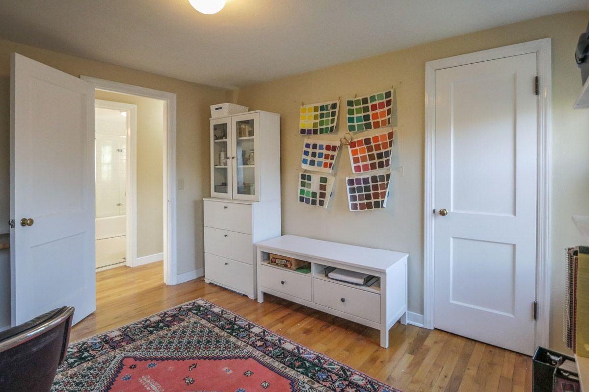 Interior room with colorful fabric swatches, white storage furniture, hardwood floors, and a patterned rug.