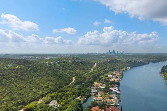 Aerial view of wooded shoreline and water with a distant city skyline.