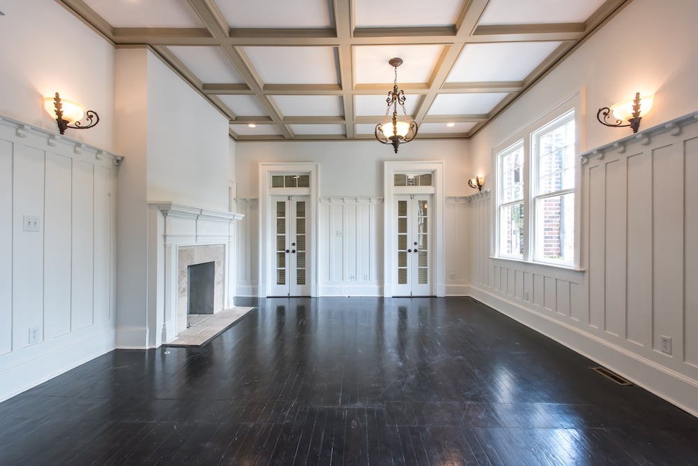 Empty formal living room with a fireplace, French doors, dark hardwood floors, and a coffered ceiling.
