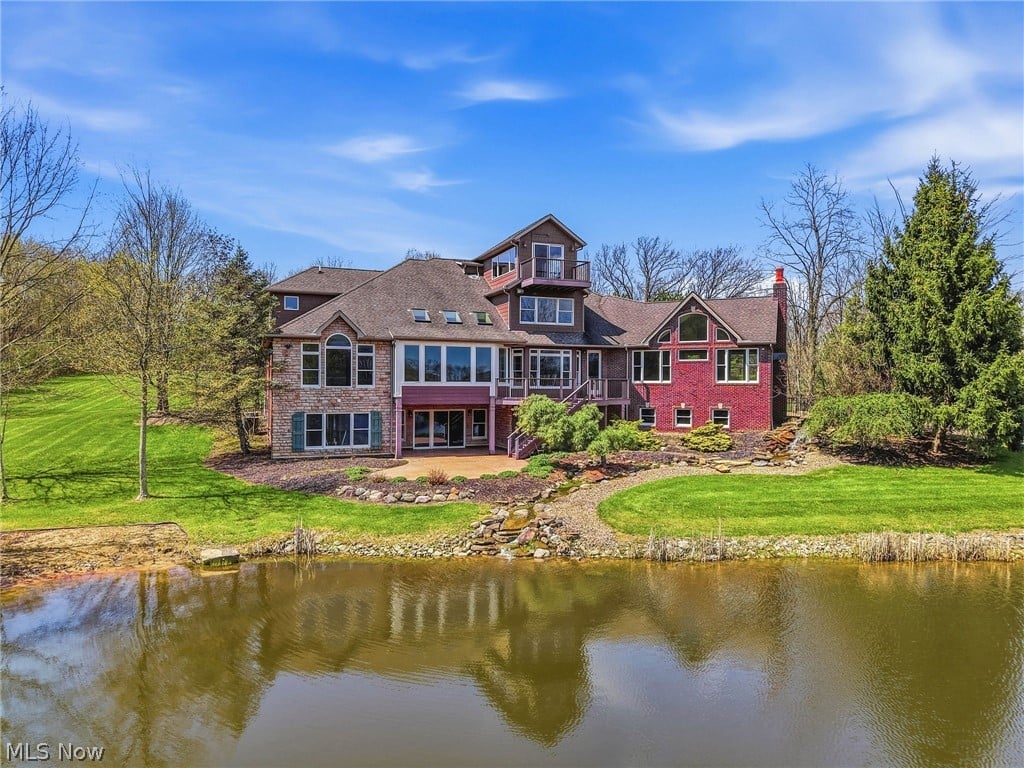 Large brick-and-stone home beside a pond, with a balcony and landscaped lawn.