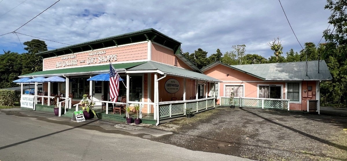 Pink commercial storefront with green trim, a covered porch, and an American flag by the entrance.