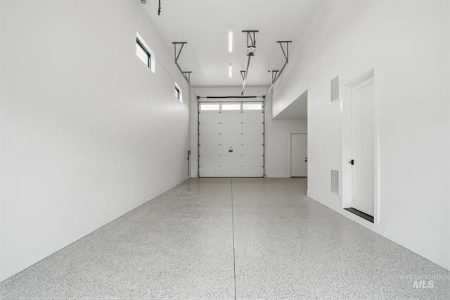 Empty white garage with a speckled floor, overhead door rails, and a side entry door.