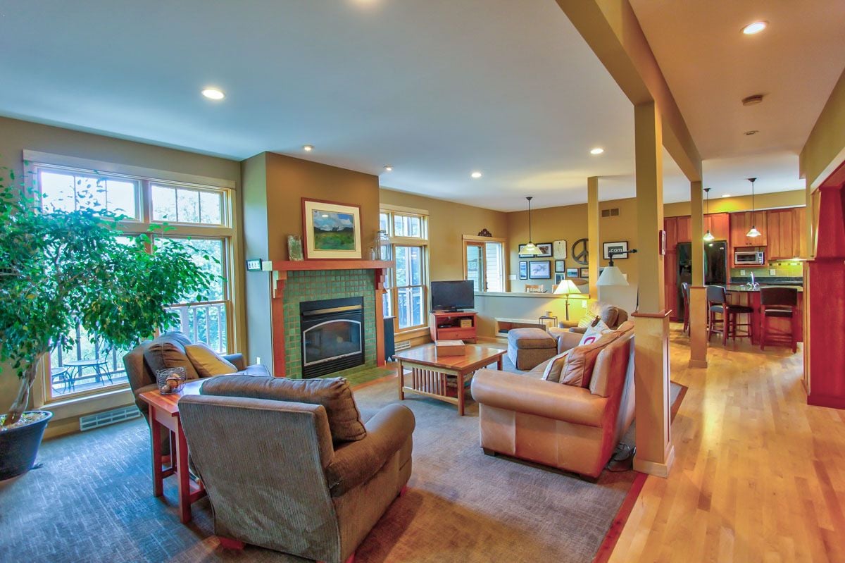 Open-plan living room with a green-tiled fireplace, large windows, and kitchen breakfast bar.
