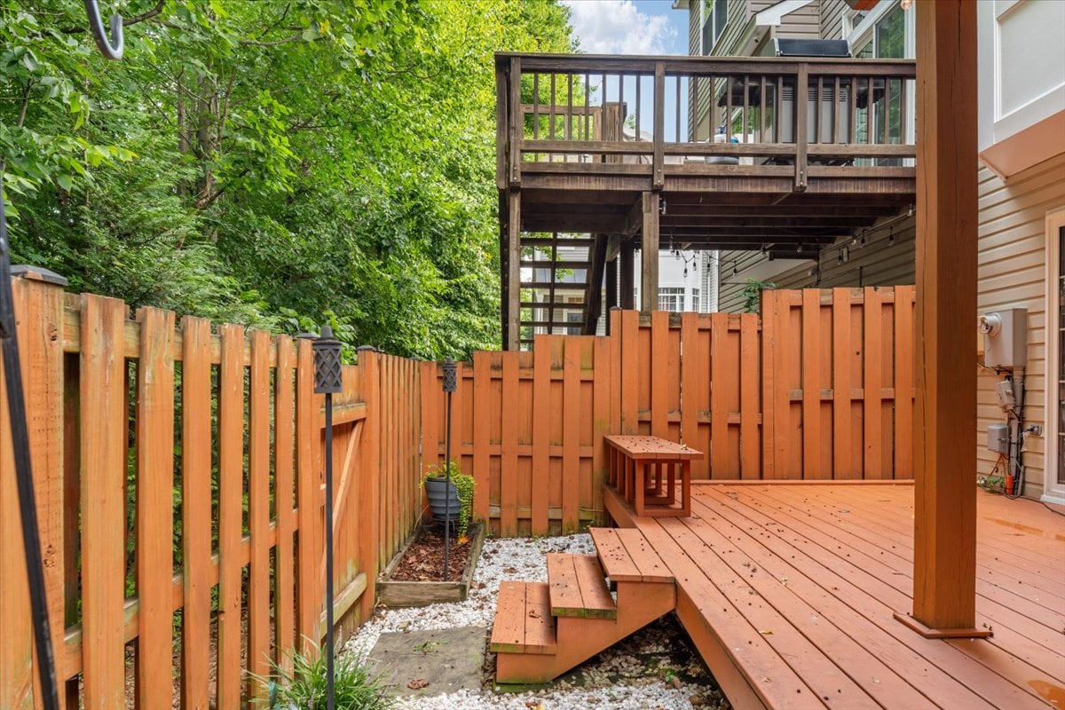 Raised wood deck with steps and a bench in a fenced, tree-lined backyard.