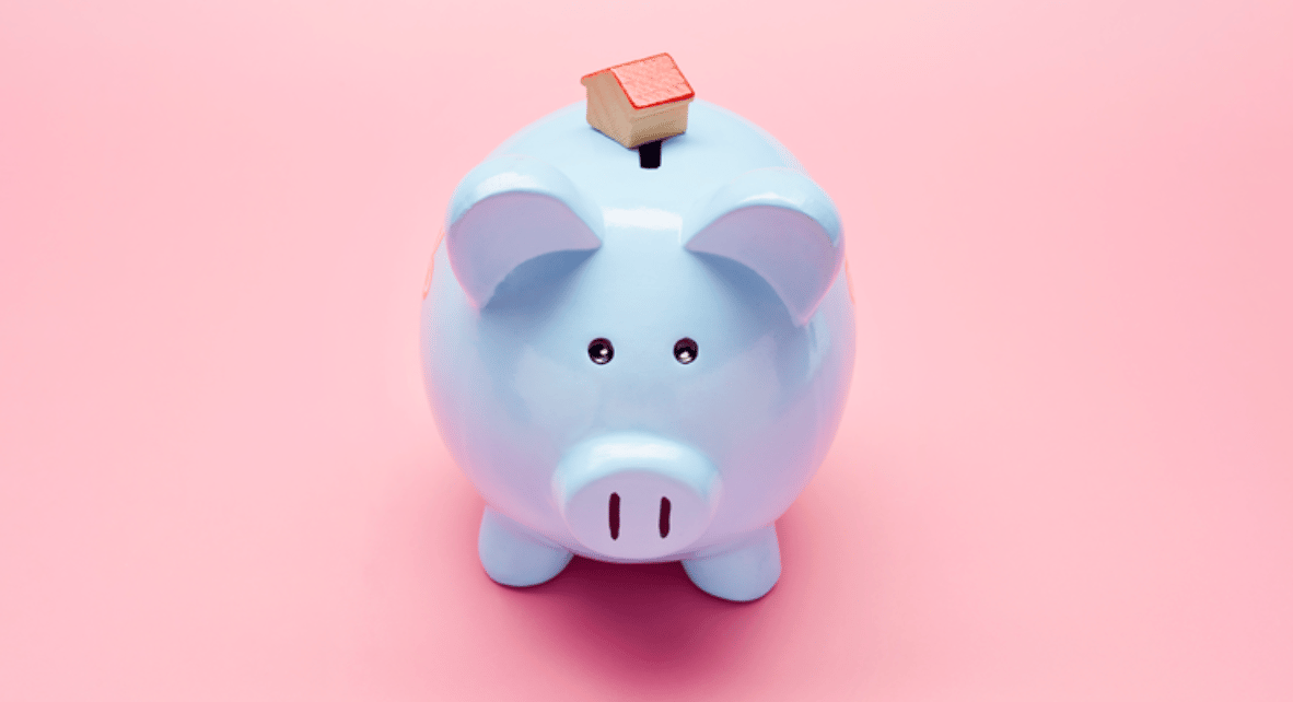 Blue piggy bank topped with a miniature house against a pink background.