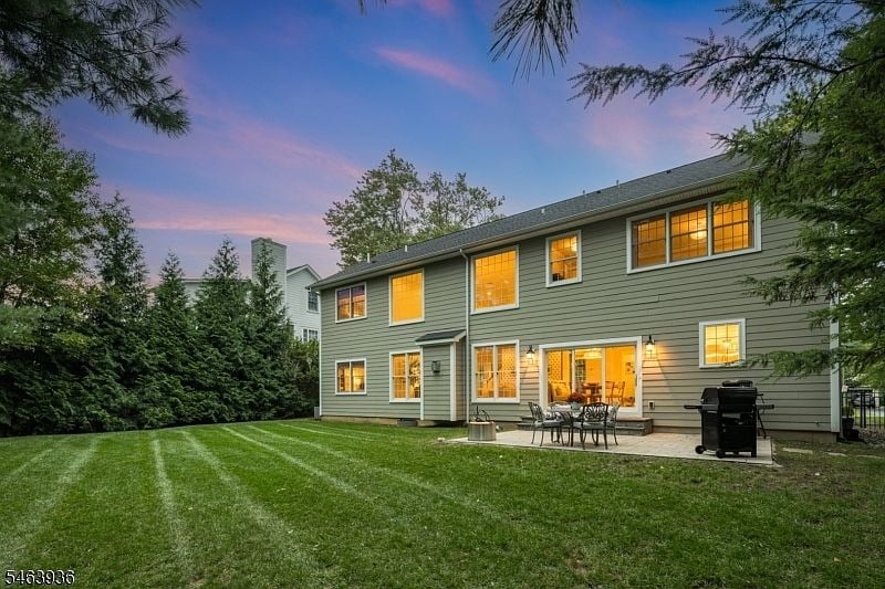 Two-story gray house at dusk, with glowing windows, a patio, and a broad lawn.