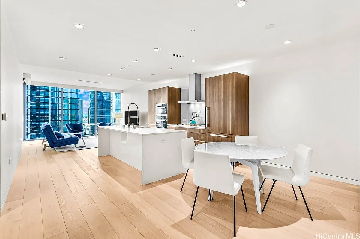 Open-plan kitchen and dining area with a large island, wood floors, and city views through floor-to-ceiling windows.