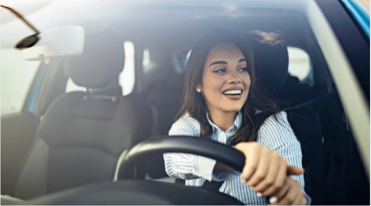 Woman smiling while driving a car in daylight.
