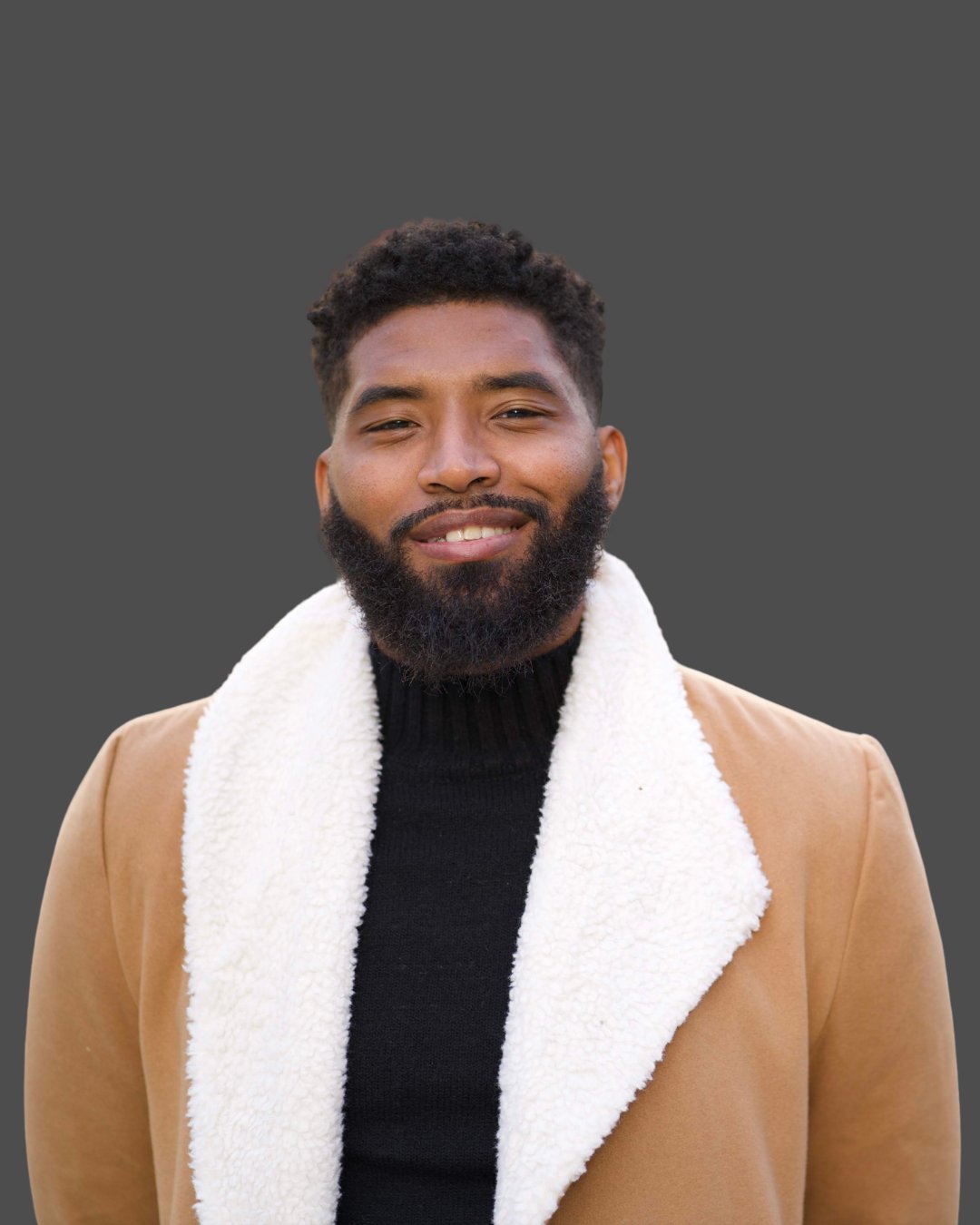Man with a full beard wearing a tan shearling-collar coat and black sweater