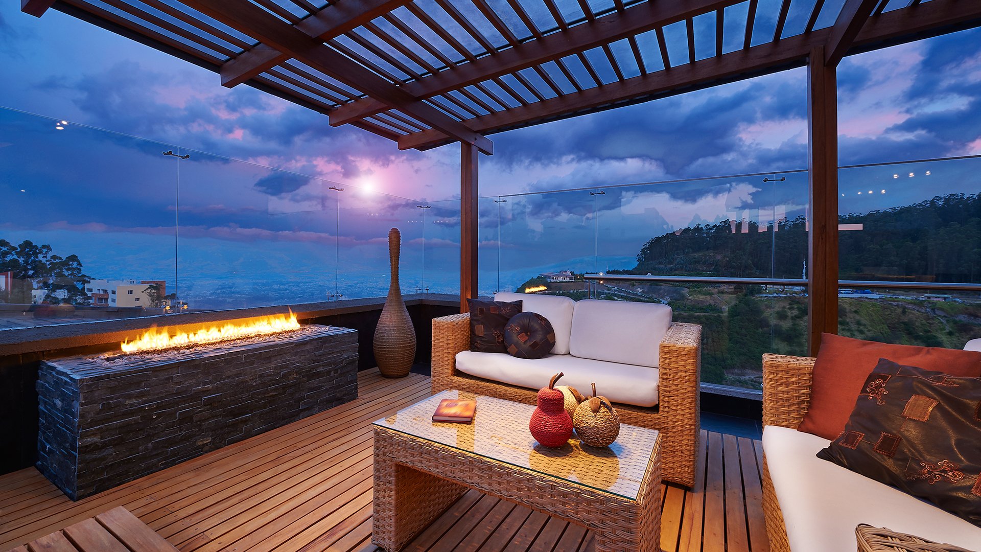 Outdoor terrace with wicker seating, a linear fire feature, and a valley view at dusk.