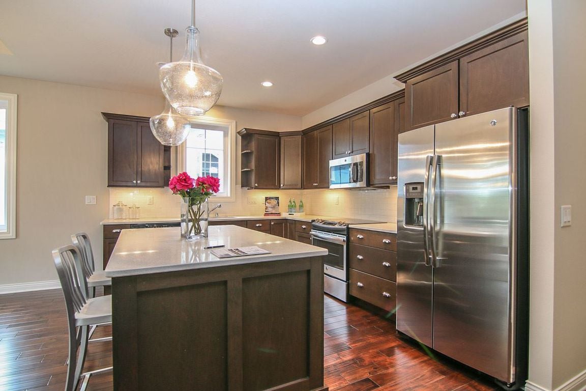 Kitchen with a large island, dark wood cabinets, stainless steel appliances, and red flowers.