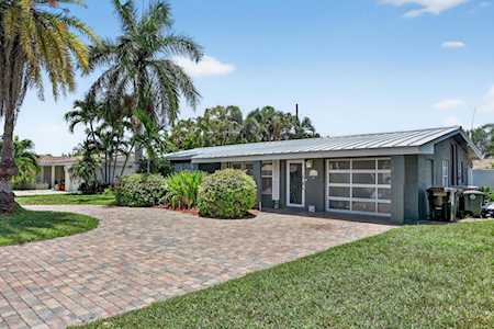 Single-story gray house with an attached garage, brick-paver driveway, and palm trees.