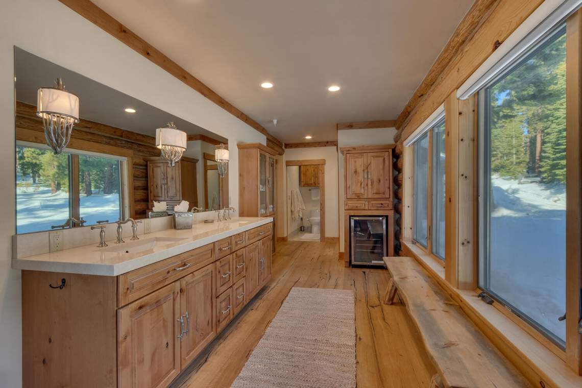 Rustic bathroom with a long double vanity and tall windows overlooking snow-covered trees.