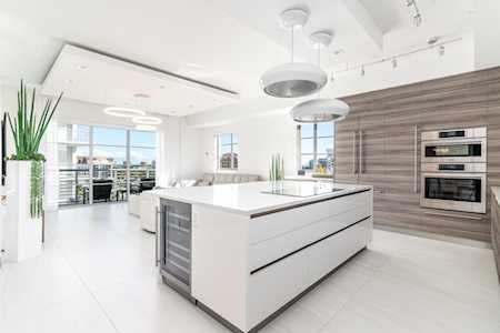 Modern white kitchen with a large island, built-in ovens, and sliding glass doors to a patio.