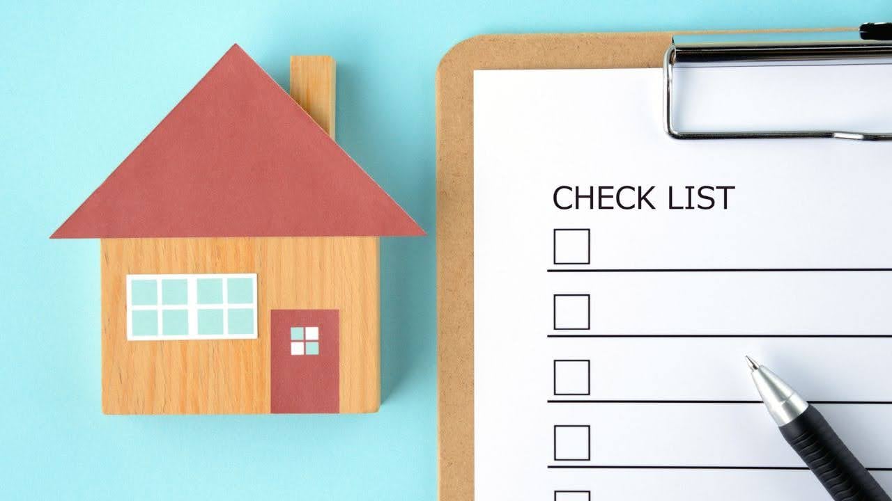 a-small-wooden-house-icon-with-a-red-roof-sits-beside-a-clipboard-with-a-checklist-and-a-pen-set-against-a-light-blue-background