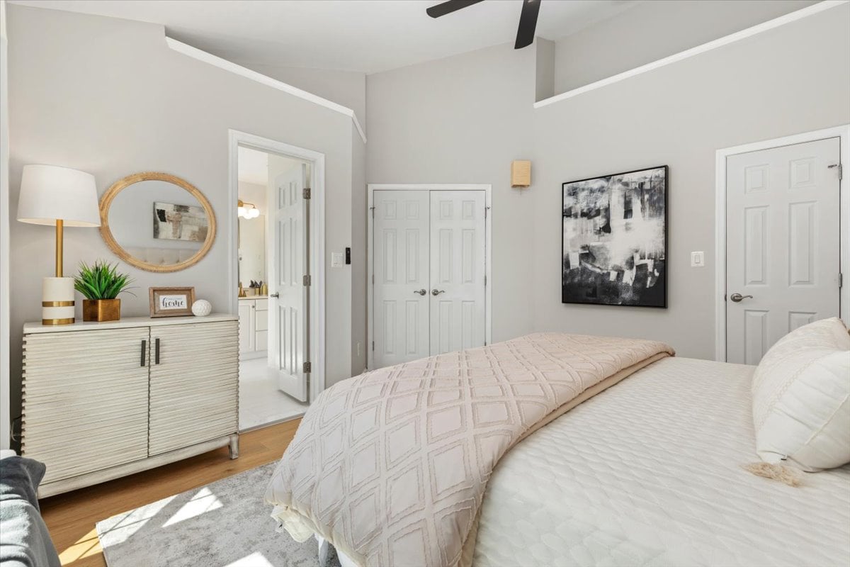 Bright bedroom with a white bed, blush quilt, ribbed dresser, and high ceiling.