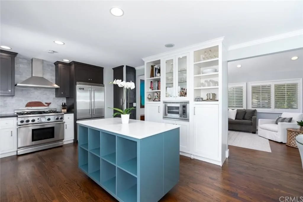  A spacious kitchen with dark and white cabinets, a large blue island, and a stainless steel range and refrigerator.