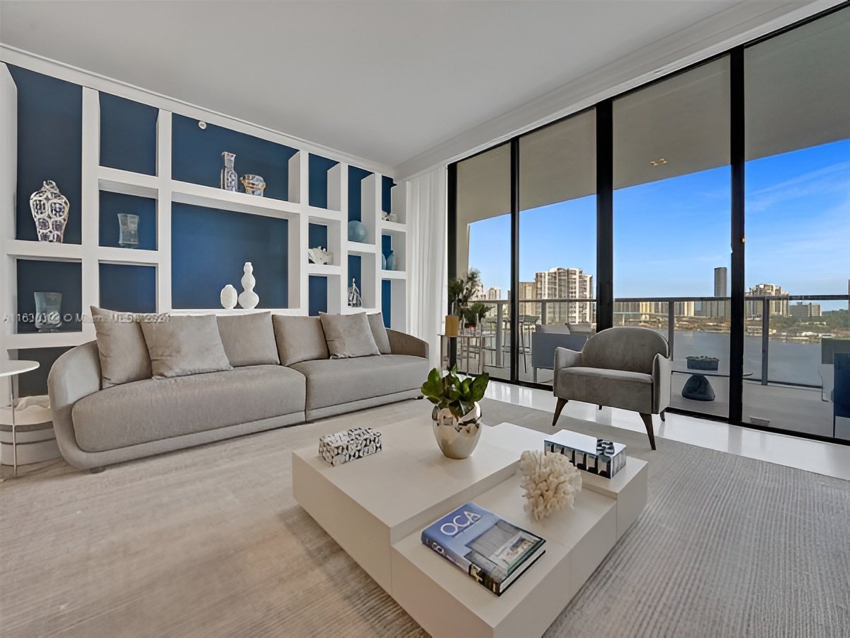 Modern living room with blue display shelves and floor-to-ceiling windows overlooking the water and city.