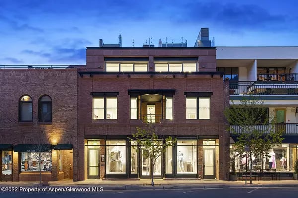 Brick commercial building with illuminated storefronts and balconies at dusk.