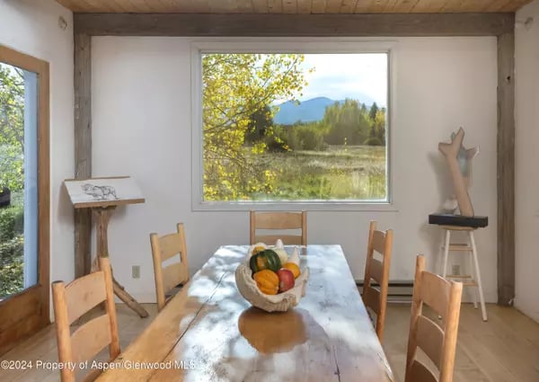Dining room with a long wooden table and chairs overlooking autumn foliage and distant mountains.