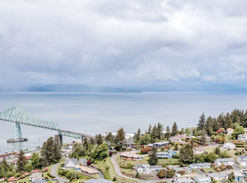 Aerial view of the Astoria-Megler Bridge, Columbia River, and hillside homes under a cloudy Pacific Northwest sky