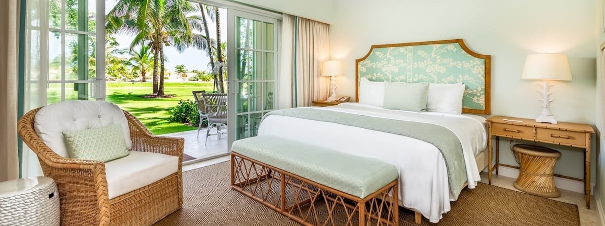 Bedroom with an aqua patterned headboard and open doors overlooking a palm-lined garden.