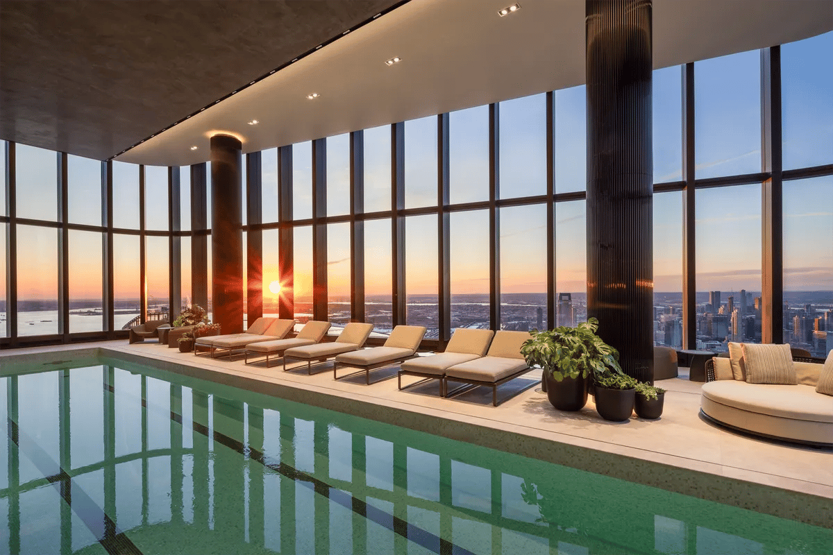 Indoor pool and lounge with floor-to-ceiling windows overlooking the city at sunset.