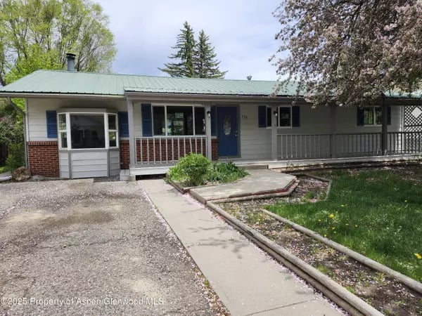 Single-story home with a covered porch, pale green metal roof, blue door, and concrete walkway.