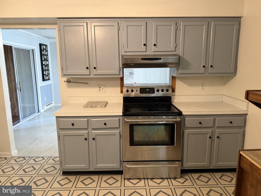 Kitchen with gray cabinets, stainless steel range, light countertops, and patterned geometric floor tile.