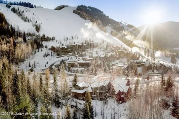 Snow-covered Aspen homes scattered among evergreen trees on a mountain slope.