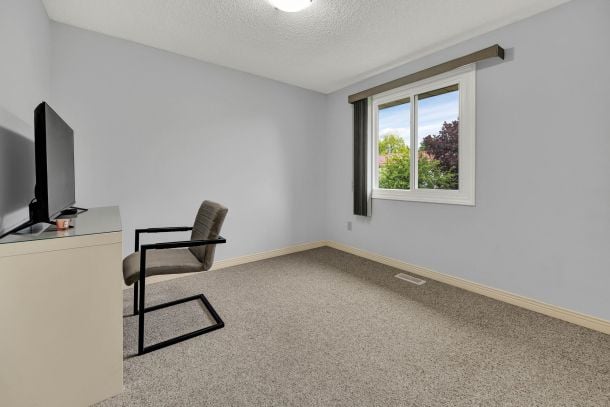 Carpeted home office with a chair, television, and window overlooking trees.