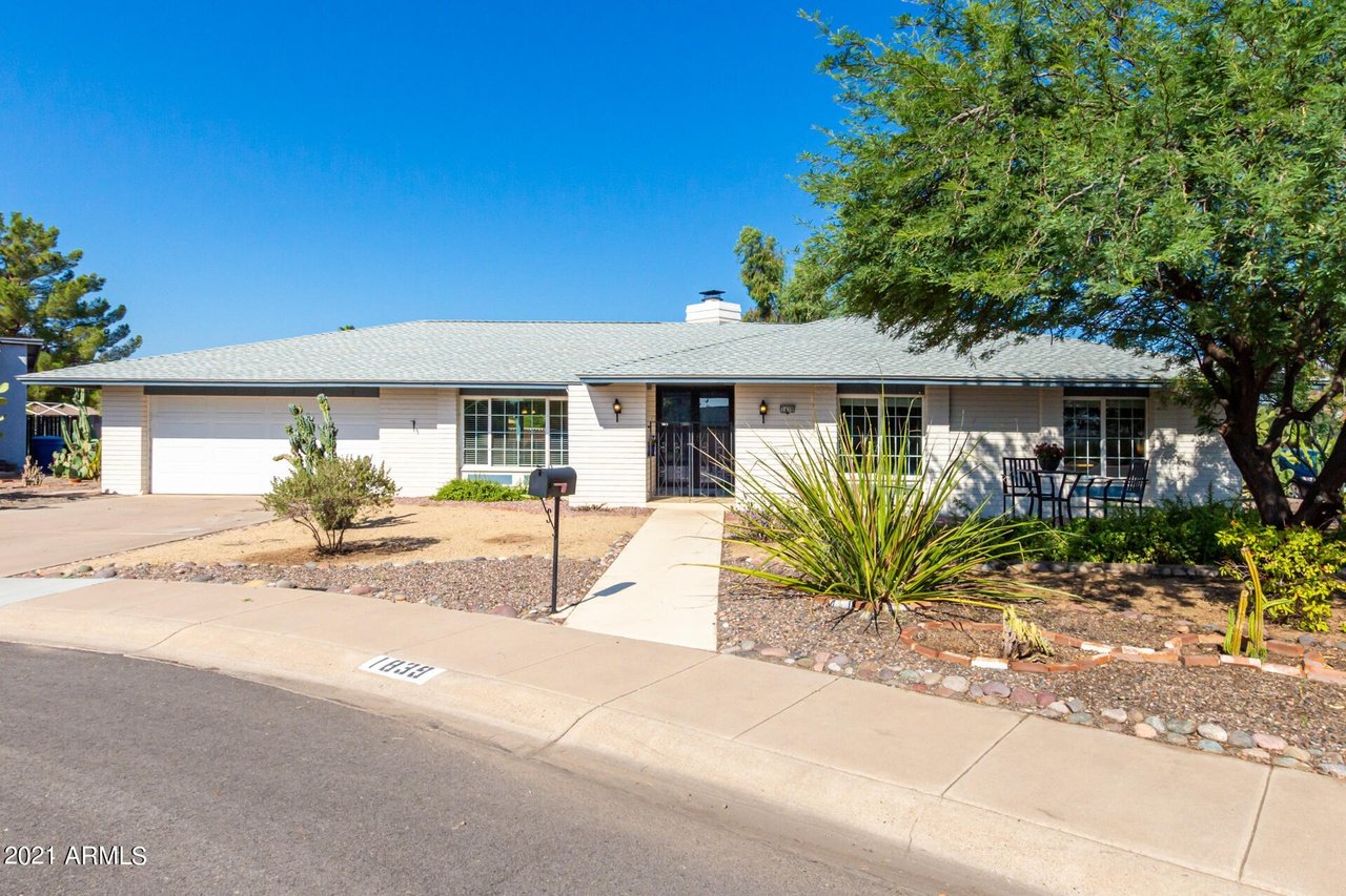 Single-story home with an attached garage, desert landscaping, and shaded patio seating.