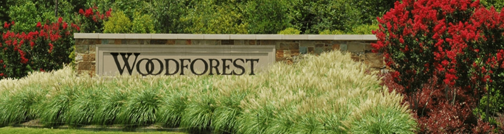 Woodforest entrance sign framed by ornamental grasses and red flowering trees.